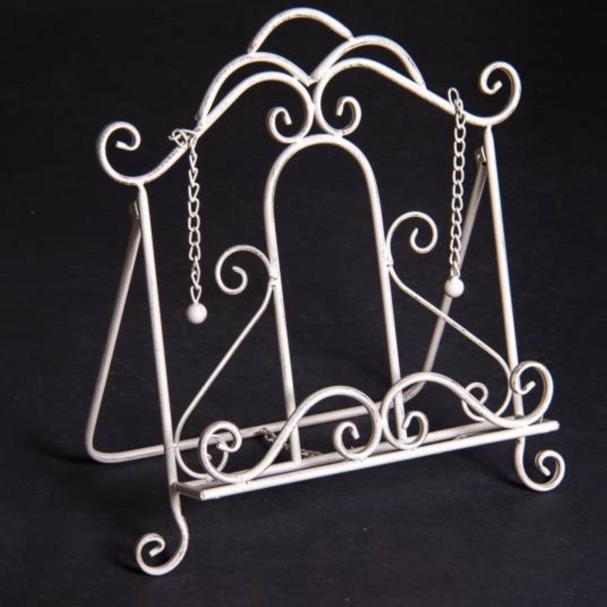 A white metal book stand with decorative elements and small chains.
