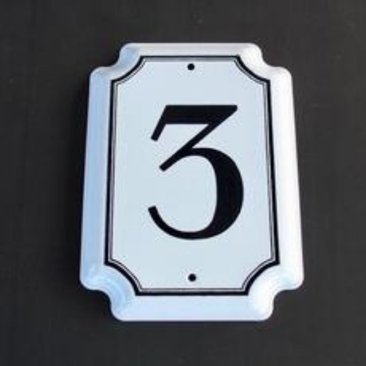 Traditional white enamel house number with the numeral  in black, with a  white border and screw holes visible.