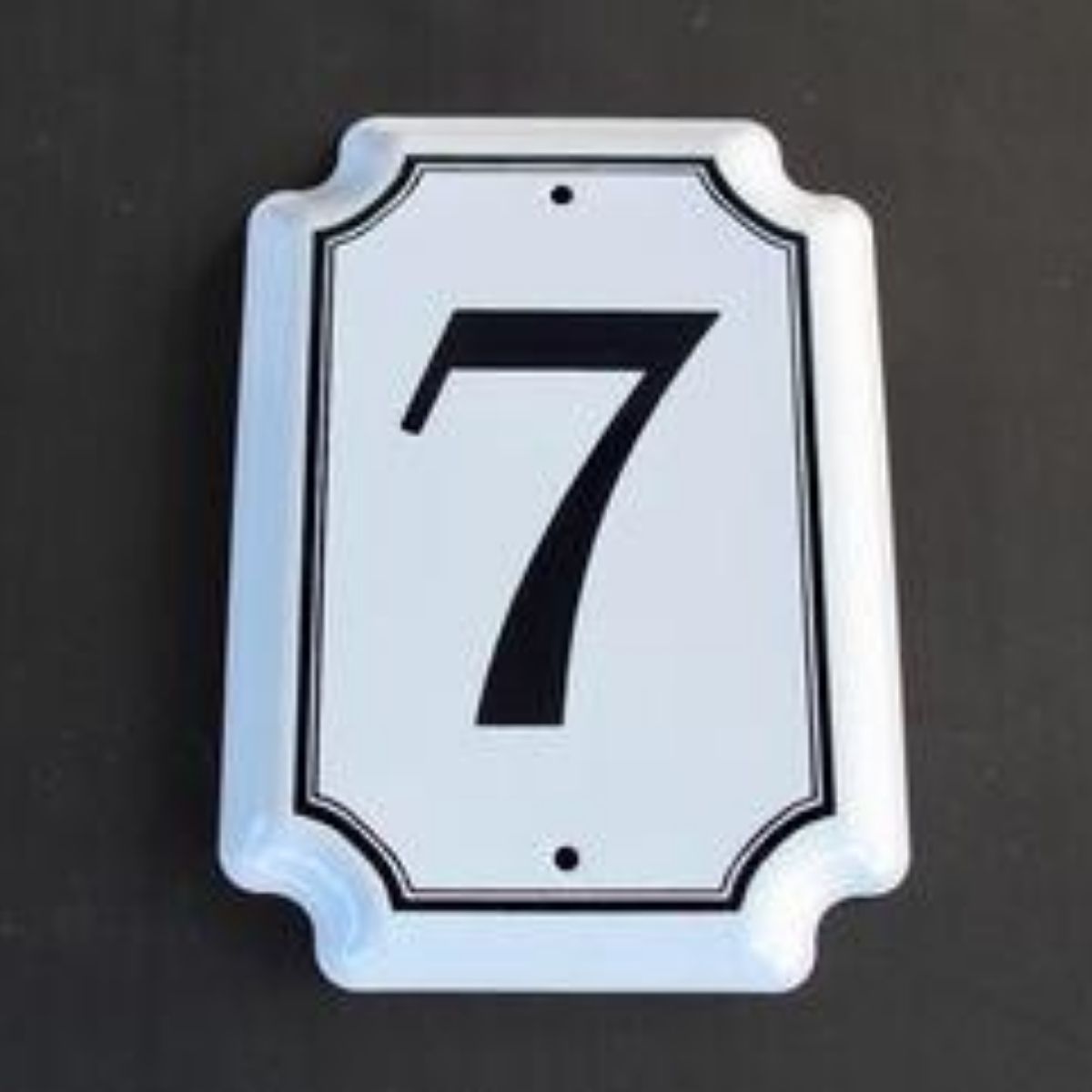 Traditional white enamel house number with the numeral  in black, with a  white border and screw holes visible.